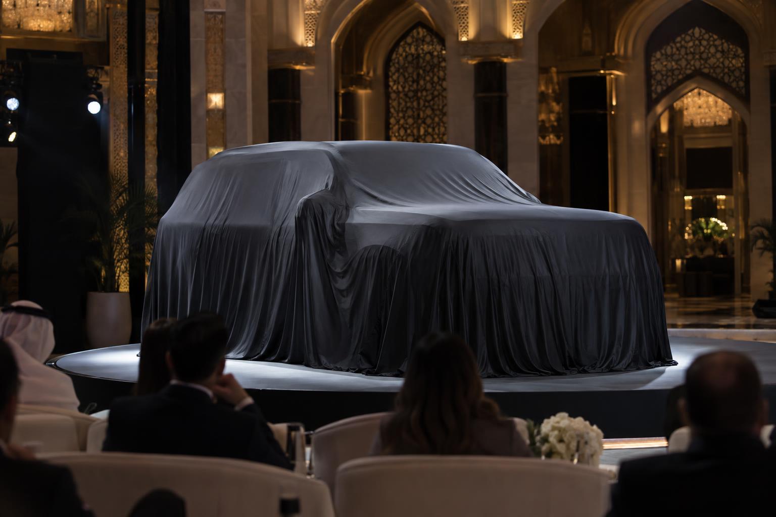 A covered SUV on a formal indoor reveal stage with a small audience.