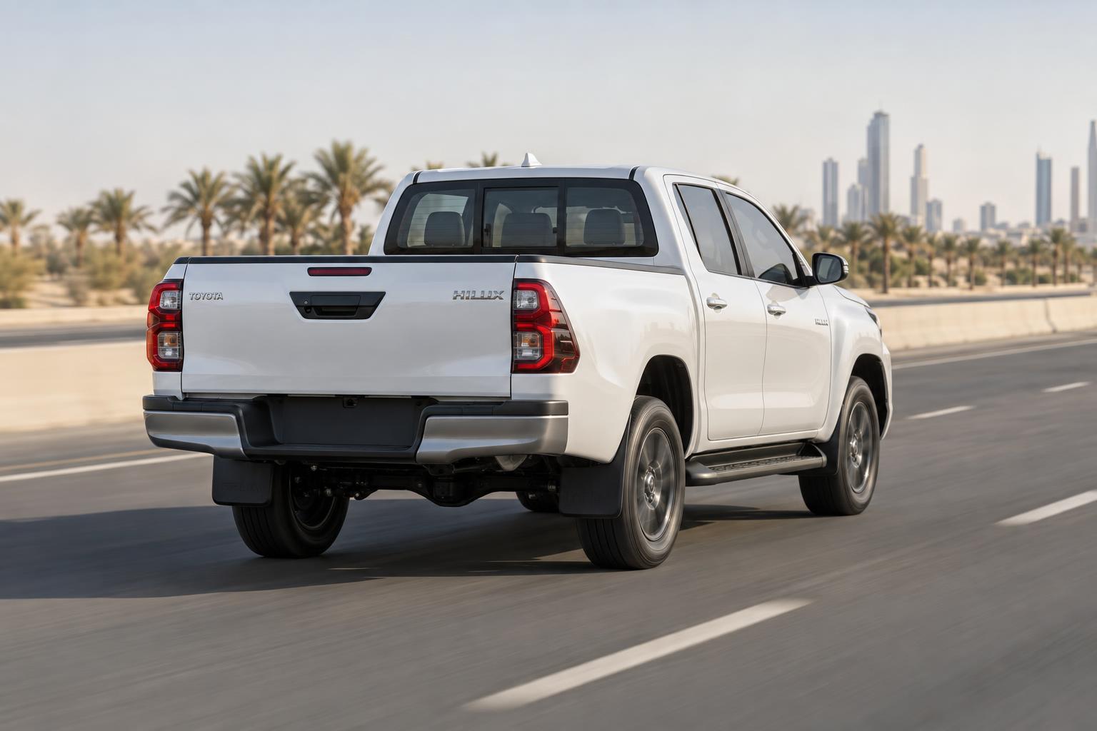 Ninth-generation Toyota Hilux driving on a Saudi highway in a rear three-quarter view.
