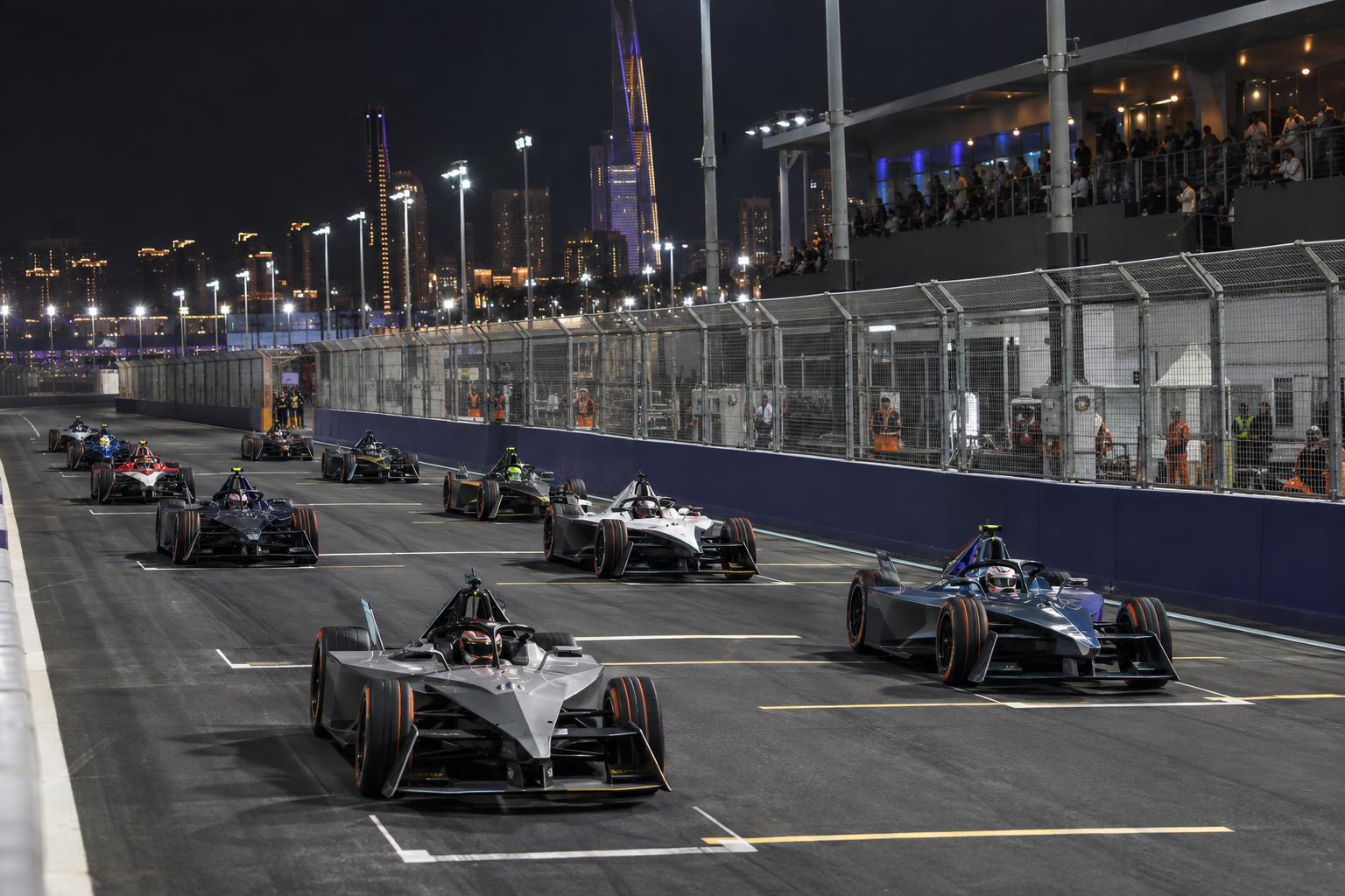 Formula E GEN4 cars line up on the floodlit Jeddah Corniche Circuit grid.