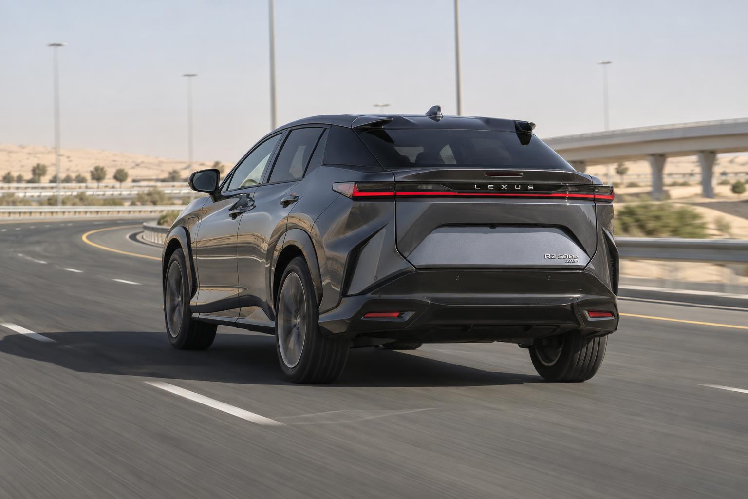 Lexus RZ 500e rounding a dry UAE highway curve from the rear three-quarter angle.