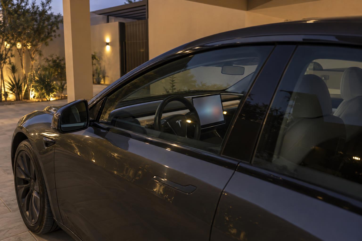 A Tesla Model 3 parked at home with its cabin display illuminated for a remote software update.
