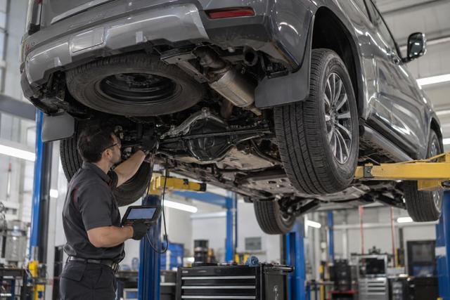 A technician inspecting the underside of a raised Nissan Patrol Y63 in a workshop.