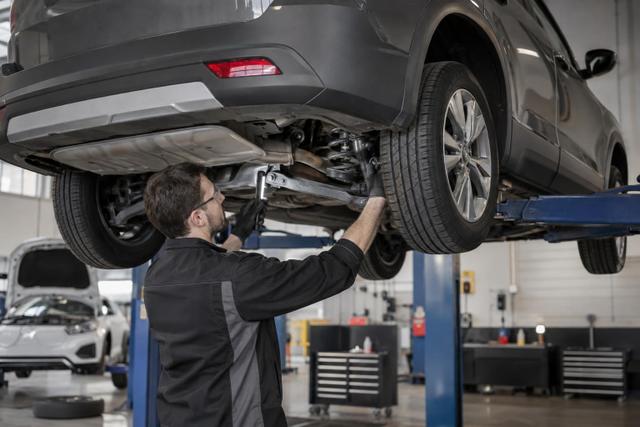 Technician inspecting the underside and wheel area of a crossover on a workshop lift.