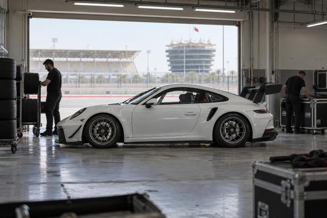A Porsche Cup car and mechanics in a quiet, partially packed pit garage.