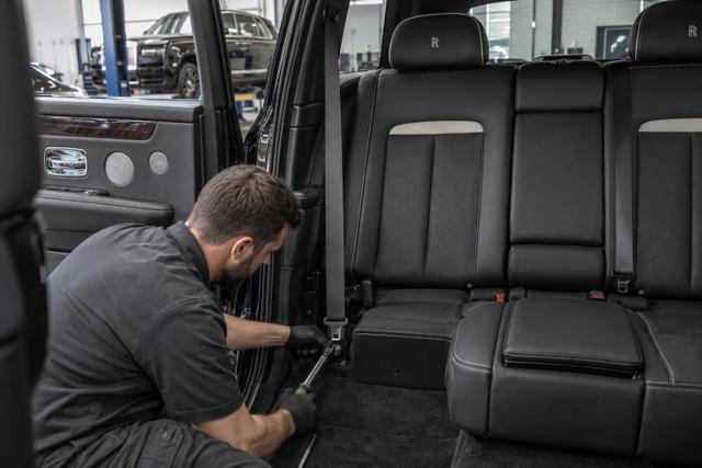 A technician inspecting rear seat-belt mounting hardware in a Rolls-Royce Cullinan.