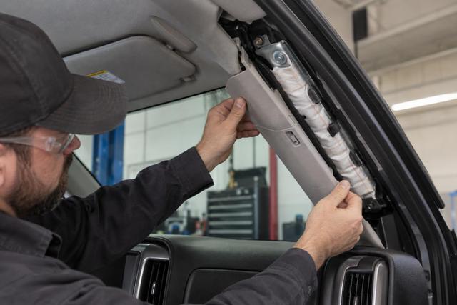A technician examining the roof-rail curtain-airbag area inside a pickup truck.